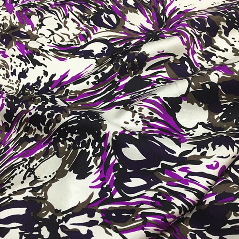 Zoom sur les plis d'une soie de mûrier au motif abstrait violet, noir et beige avec une brillance satinée.