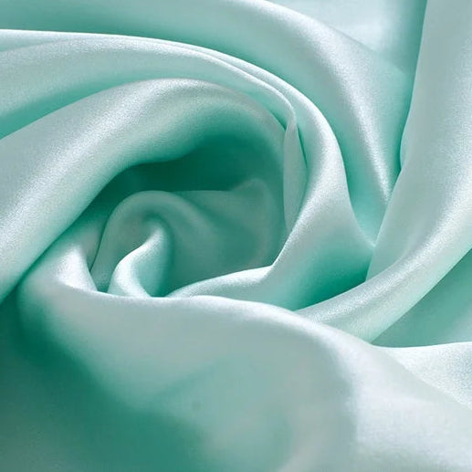 Zoom sur un tissu en soie de mûrier vert eau aux reflets nacrés, texture douce et fluide pour articles de nuit de luxe.